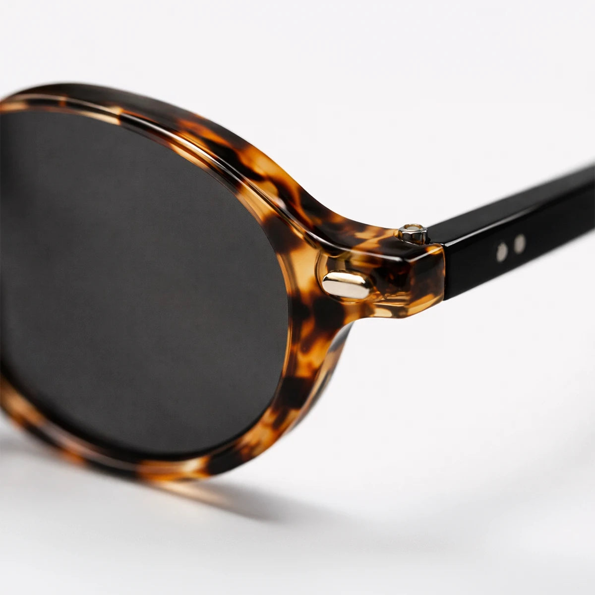 Gafas de sol redondeadas London Carey con montura de carey ámbar, patillas negras y lentes gris ahumado.
