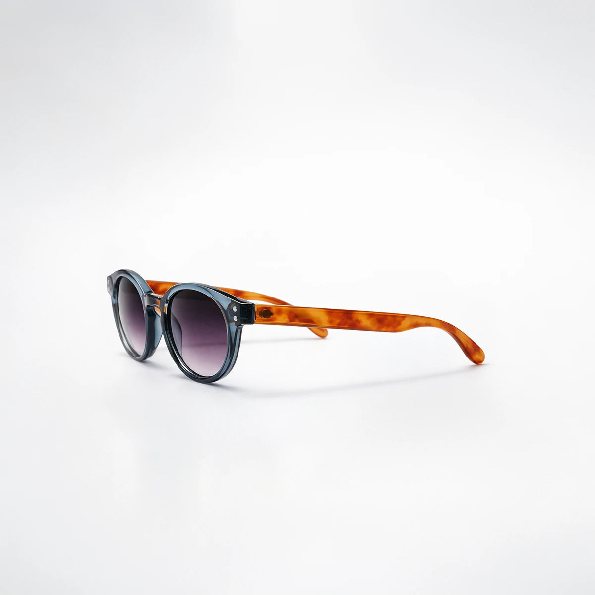 Gafas de sol redondeadas Paris Fade con montura azul translúcida, patillas de carey ámbar y lentes en degradado violeta.
