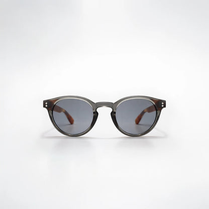 Gafas de sol redondeadas Paris Noir con montura negro translúcido, patillas de carey ámbar y lentes gris oscuro.
