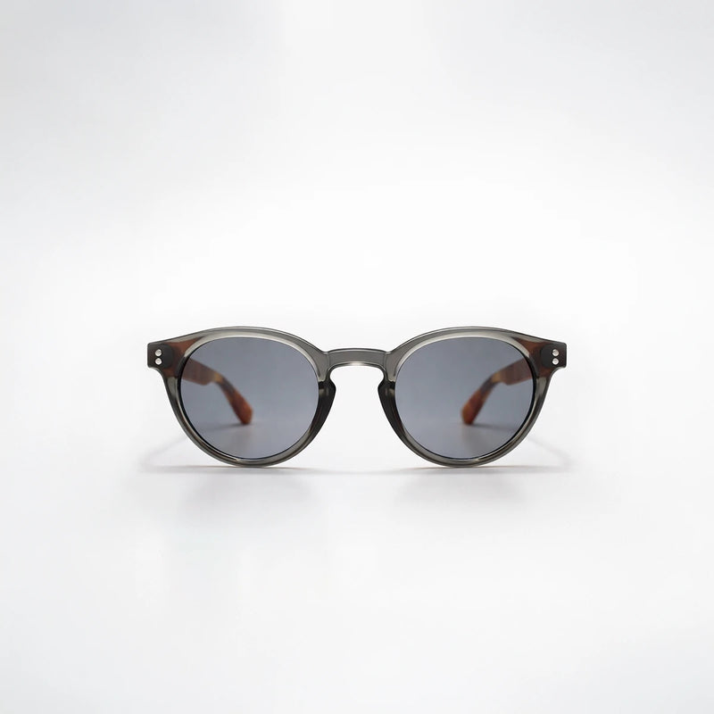 Gafas de sol redondeadas Paris Noir con montura negro translúcido, patillas de carey ámbar y lentes gris oscuro.
