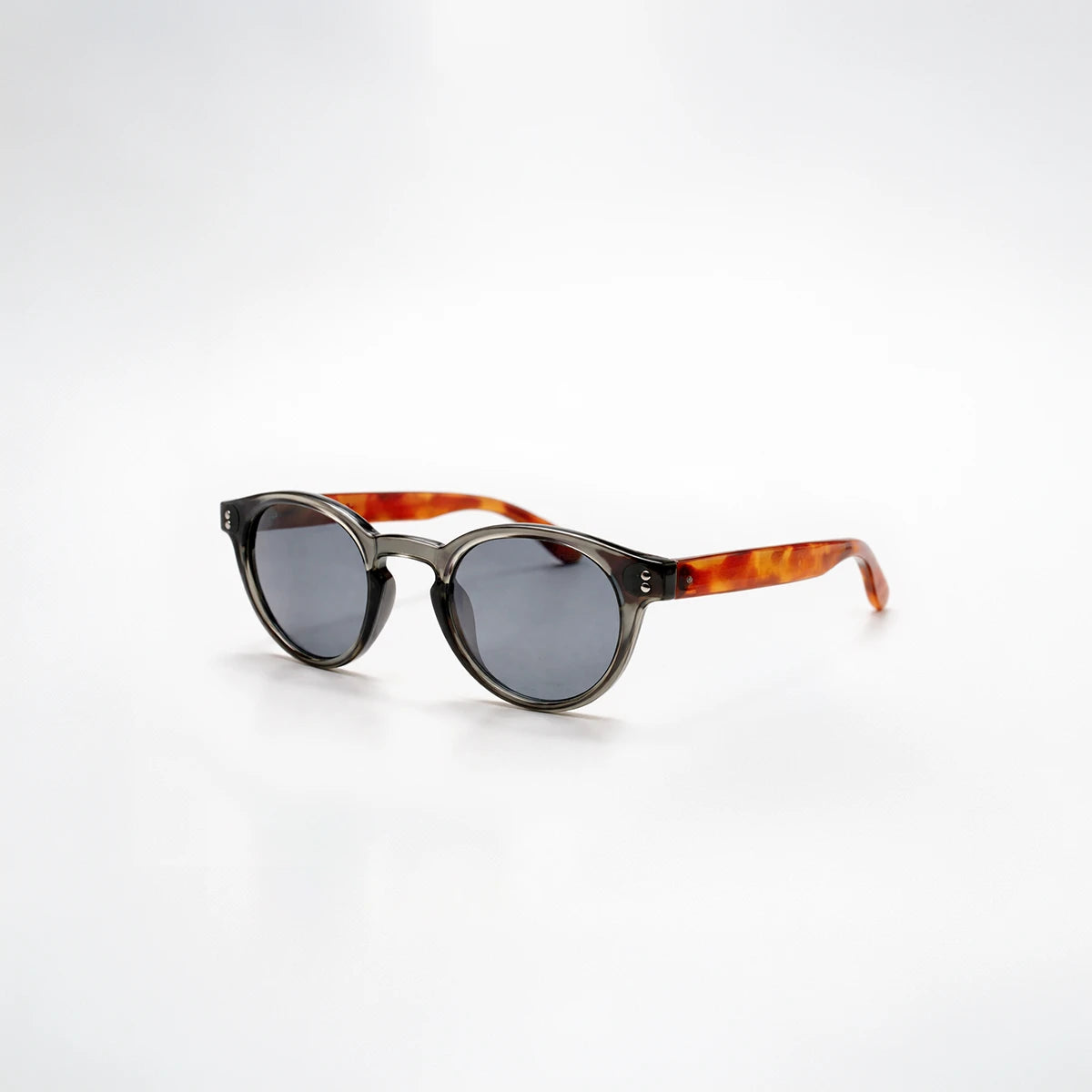 Gafas de sol redondeadas Paris Noir con montura negro translúcido, patillas de carey ámbar y lentes gris oscuro.

