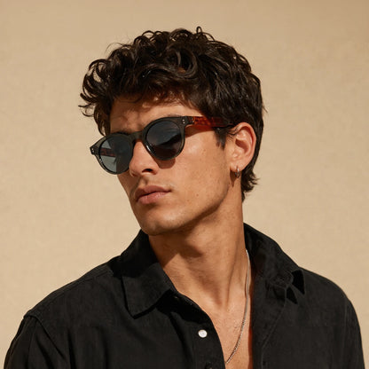 Gafas de sol redondeadas Paris Noir con montura negro translúcido, patillas de carey ámbar y lentes gris oscuro.
