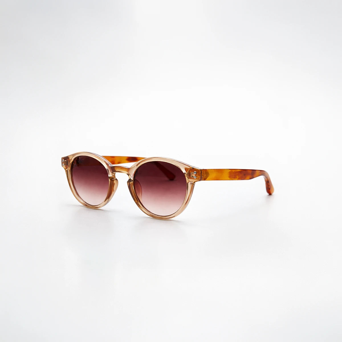 Gafas de sol redondeadas Paris Sunset con montura champagne translúcida, patillas de carey ámbar y lentes marrón rosado.
