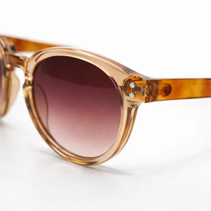 Gafas de sol redondeadas Paris Sunset con montura champagne translúcida, patillas de carey ámbar y lentes marrón rosado.
